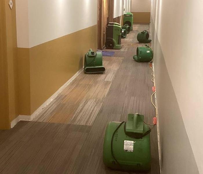Water damaged carpet in hallway is being dried using air movers